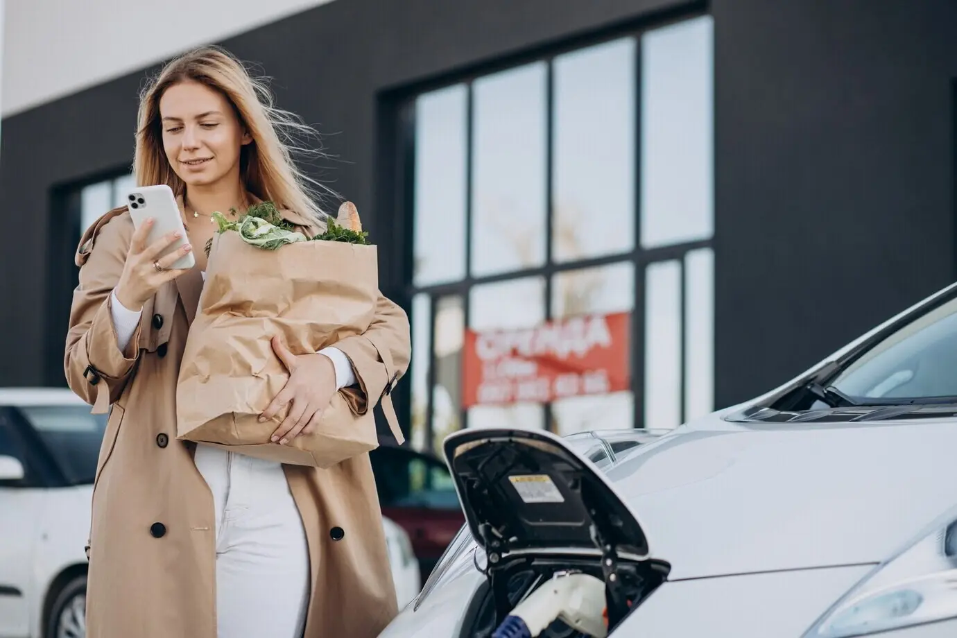A woman with grocery bags charging an electric car.
